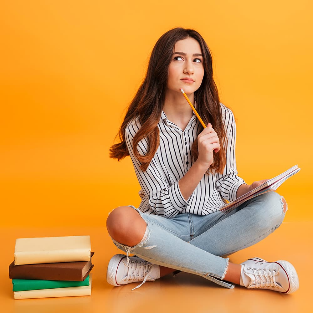 Studente zittend op de grond. Met pen en papier in de hand, aan het denken